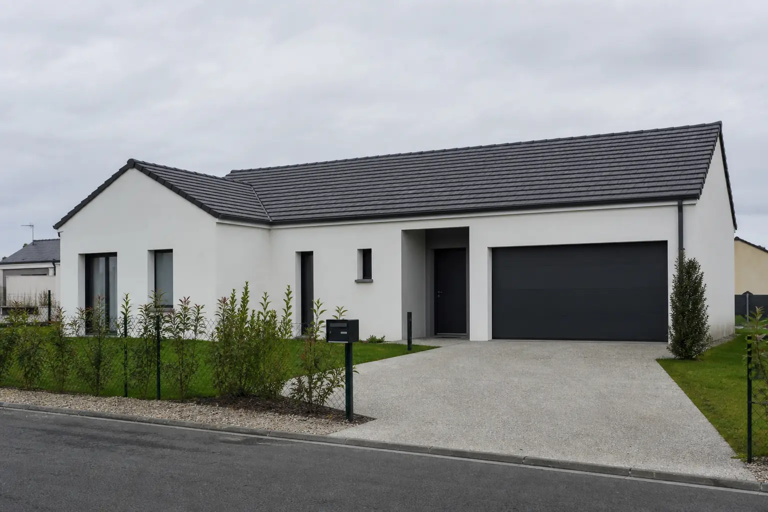 Maison individuelle récente vue de la rue, enduit blanc, menuiseries sombres et allée en béton désactivé