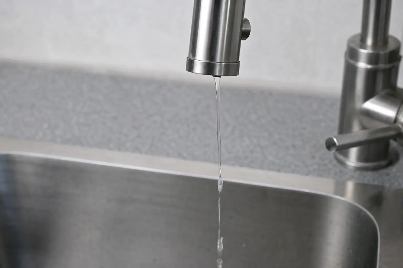 Filet d'eau faible sortant d'un robinet de cuisine en inox au-dessus d'un évier vide