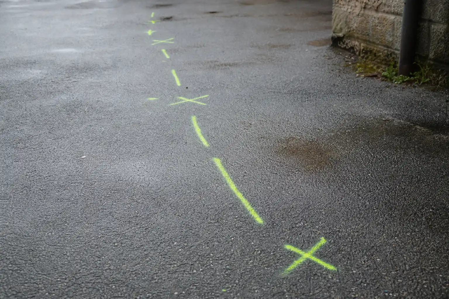 Trait et croix de peinture jaune-vert bombés sur un enrobé humide, désignant le tracé d'un réseau enterré