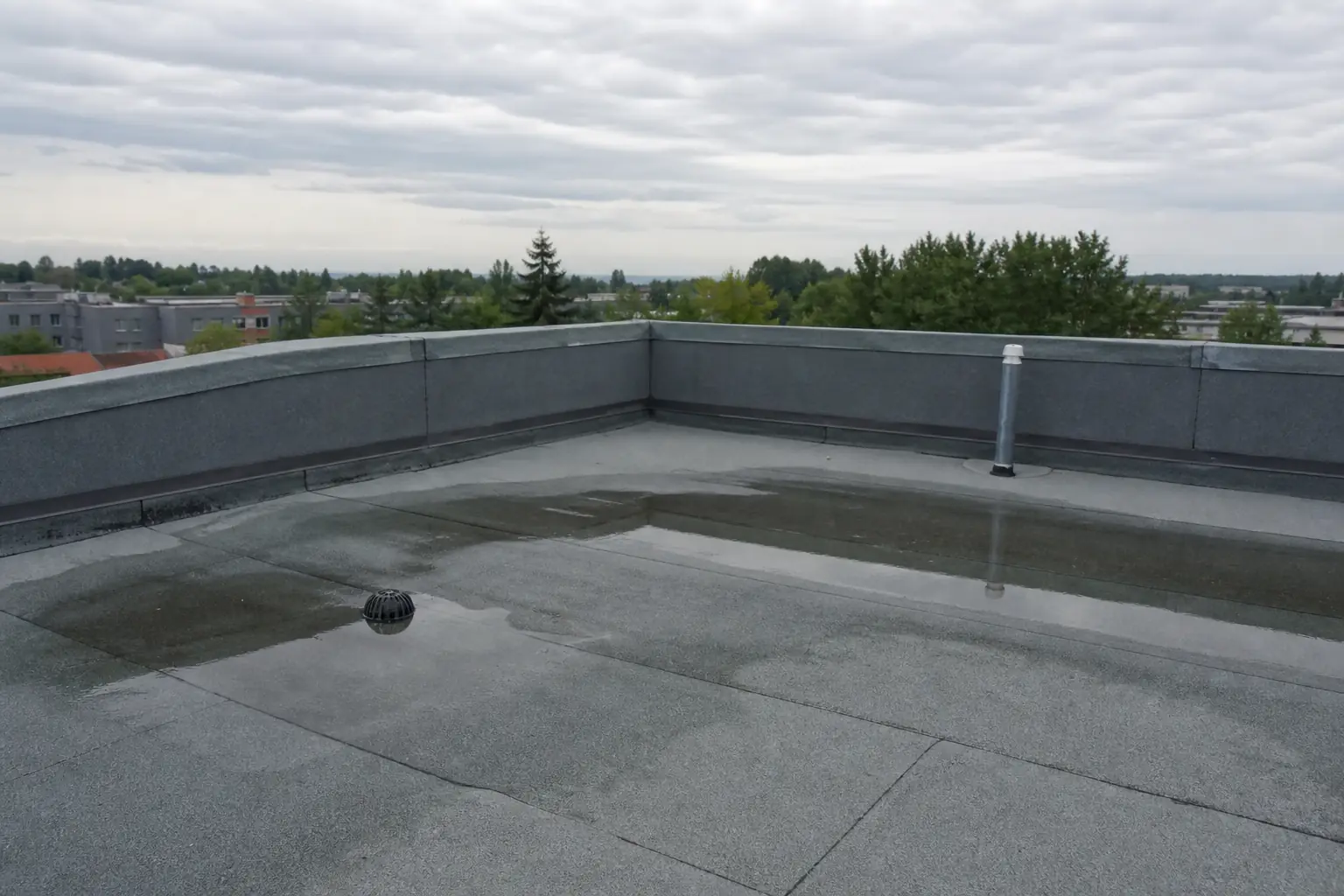 Terrasse de toit en étanchéité bitumineuse grise, relief de rive et évacuation d'eau pluviale, flaque résiduelle